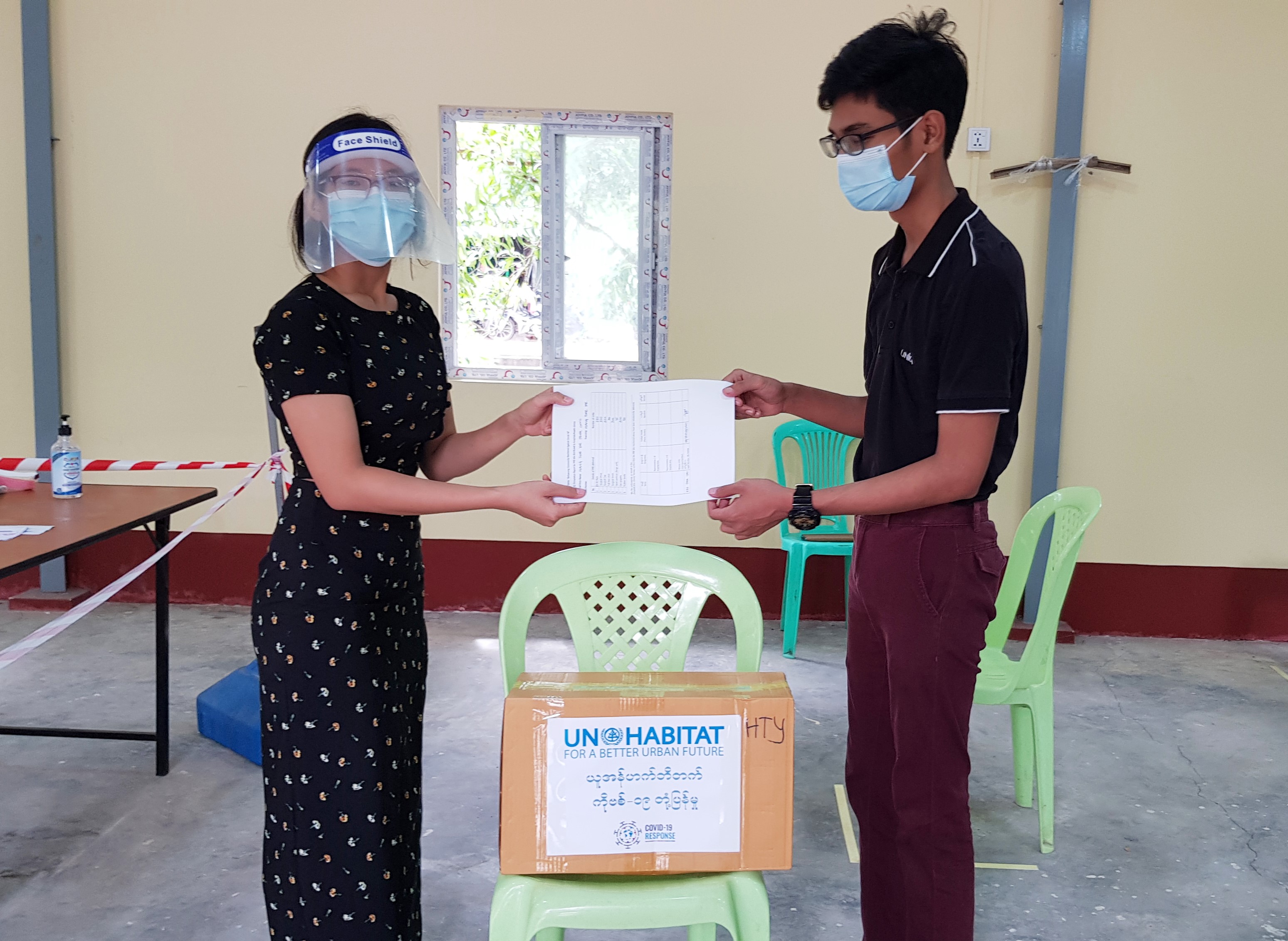 A UN-Habitat Staff member hands over the protective equipment to a representative from the Hlaingthayar fever clinic in Yangon, Myanmar to protect against COVID-19