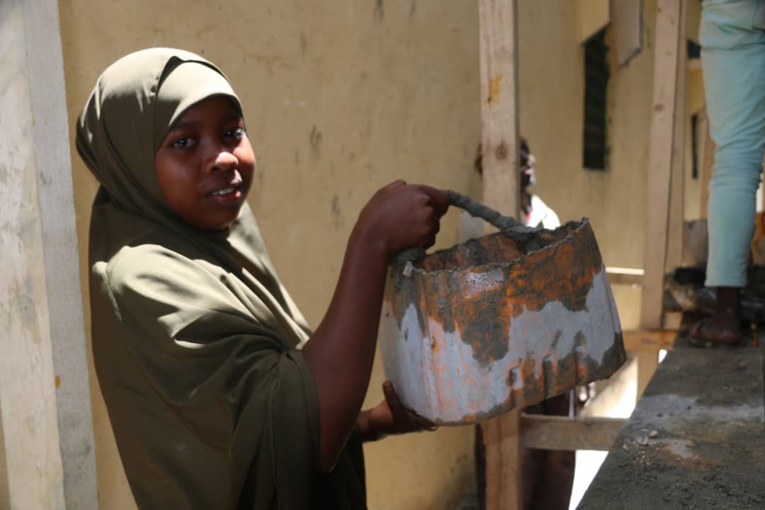 A young woman carries a bucket of cememt