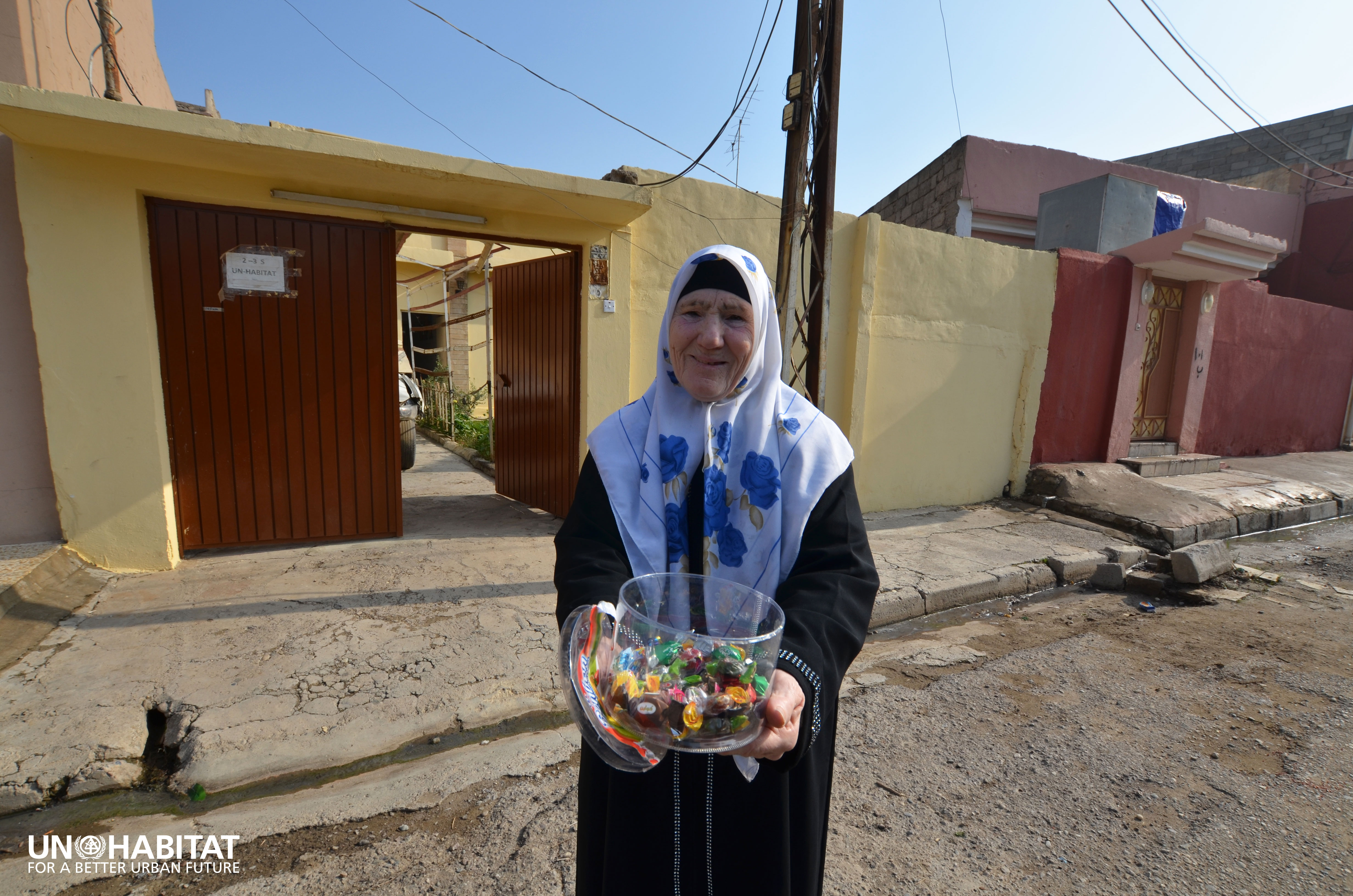 A beneficiary woman in Mosul greets the UN-Habitat team in front of her rehabilitated house 