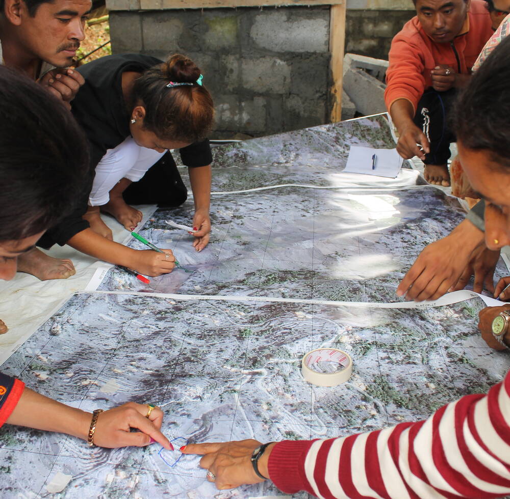 Four Nepalese residents point to a map while discussing sanitation issues.