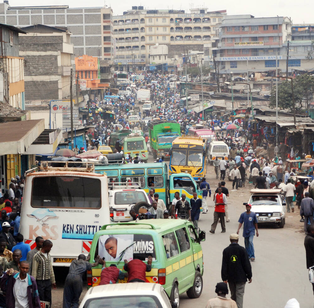 A busy Nairobi street scene showing overcrowded sidewalks, mini buses and cars. 