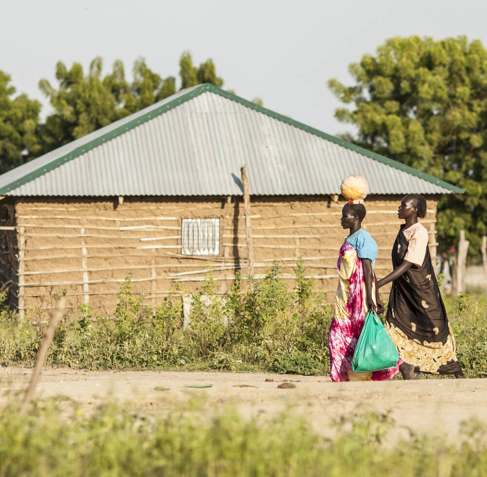 Two women walk in a village in South Sudan