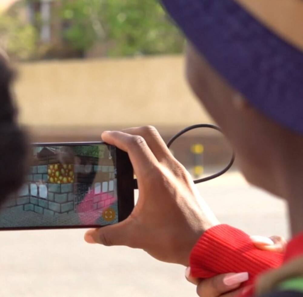 Participants in the Block by Block workshop use a phone to visualize their design in the actual public space, thus viewing their Minecraft designs in mixed reality. 