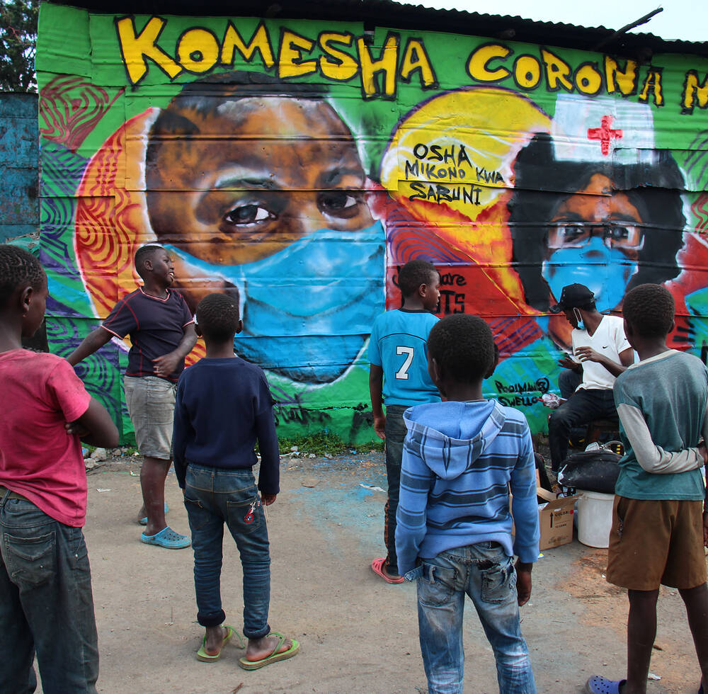 Children watch as a graffiti artist finishes one of the murals in the informal settlement of Mathare in Nairobi about COVID-19