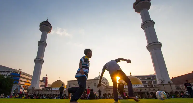Two boys play football in front of buildings.